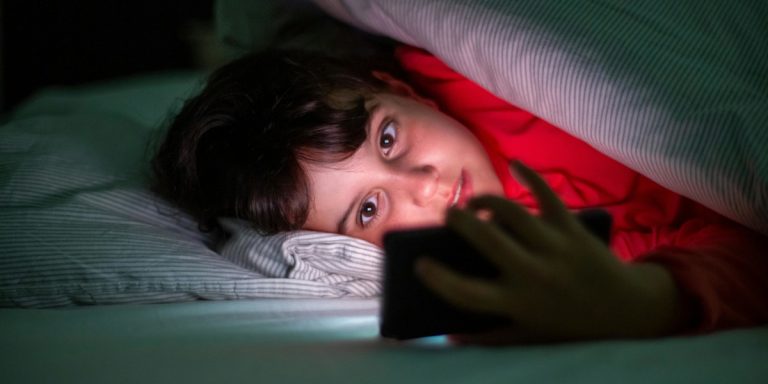 Мальчик под одеялом смотрит в телефон