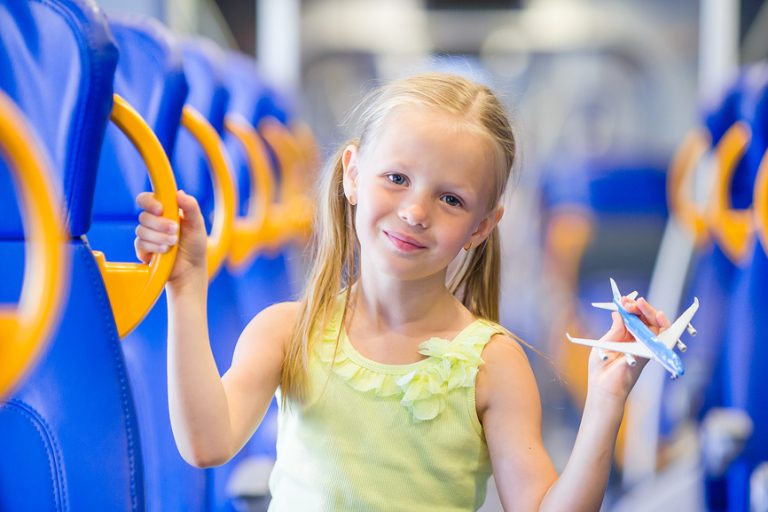 Adorable little girl traveling on train and having fun with airplane model in hands