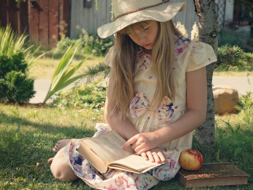 Девочка в летнем платье и шляпе читает книгу