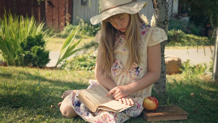 Девочка в летнем платье и шляпе читает книгу